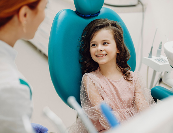 A dental assistant talking to a smiling girl in dental chair at Arlington Pediatric Dentistry, in Arlington, WA.