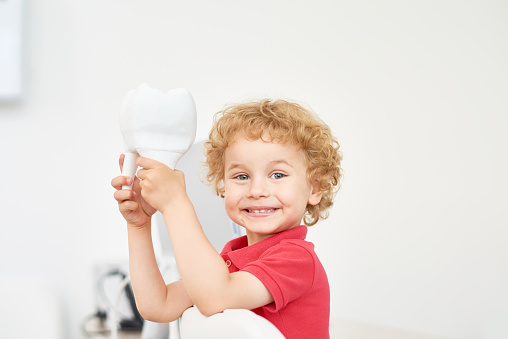 A child holding a tooth model sitting on the dental chair