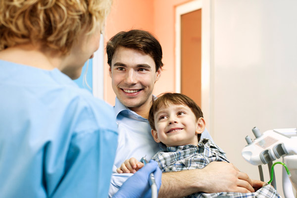 Two year old boy sitting on his dad's lap for dental exam