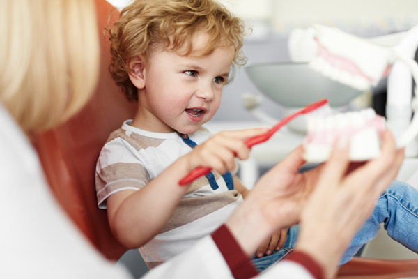 Little boy brushing teeth on dental model while sitting in dental chair, at Arlington Pediatric Dentistry in Arlington, WA.