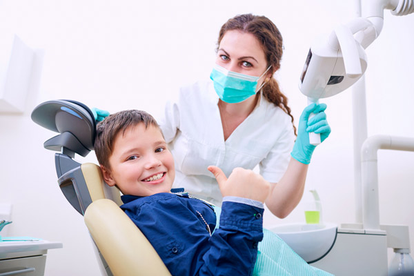 Child sitting in dental chair with doctor and giving a thumbs up, at Arlington Pediatric Dentistry in Arlington, WA.