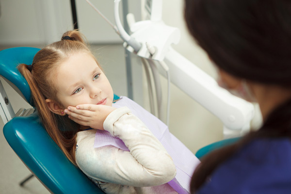 Young girl with pigtails holding her cheek due to aching tooth